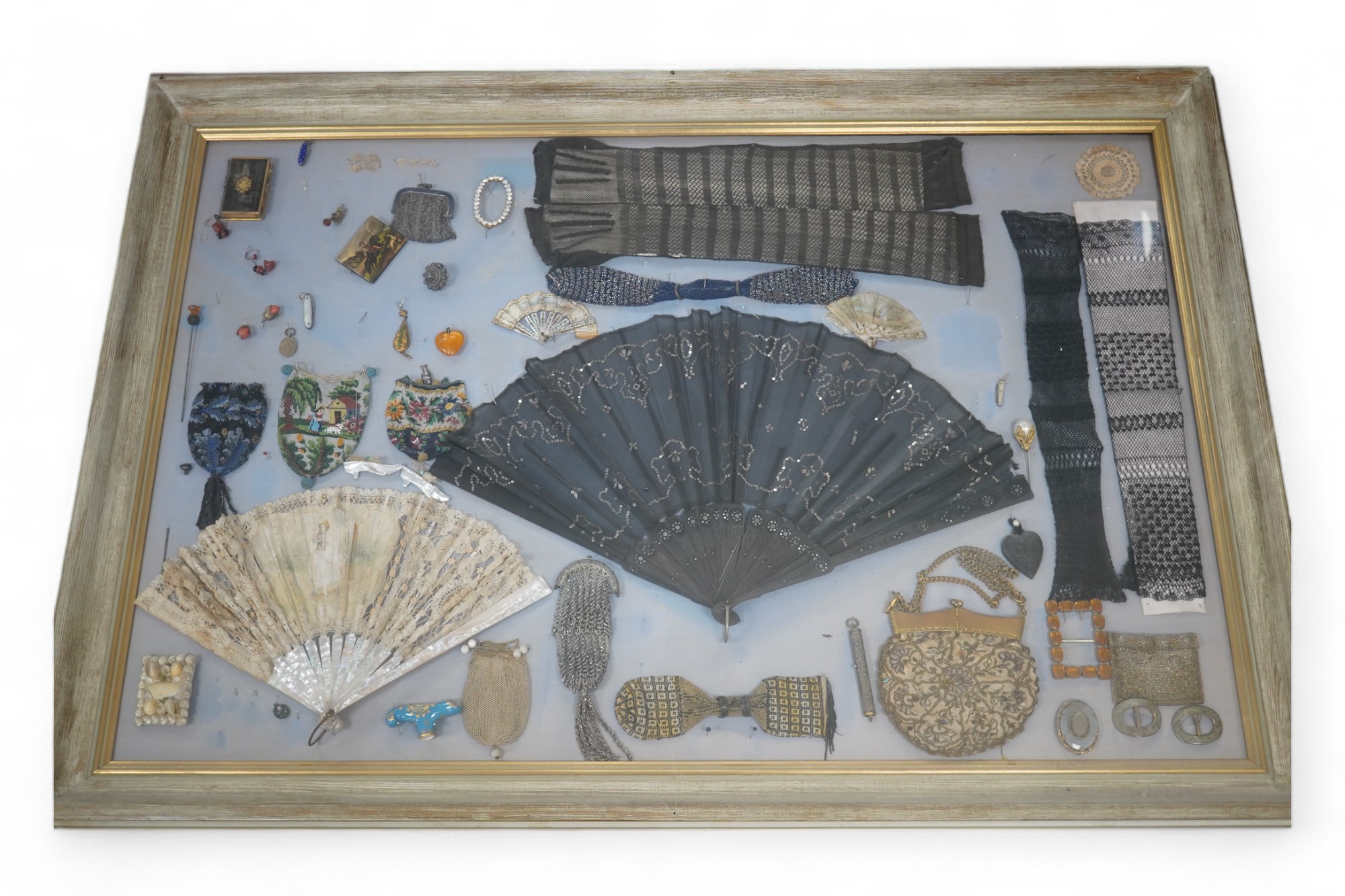 A framed display montage of late 18th and 19th century decorative ladies sequin and lace fans, beadwork reticules, cut steel misers purses, hat pins, earrings, brooches, shoe buckles and crochet mittens.100cm x 70cm. Con